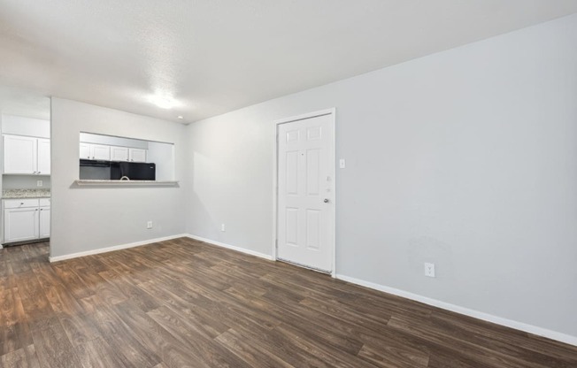 the living room and kitchen of an apartment with wood flooring and white walls