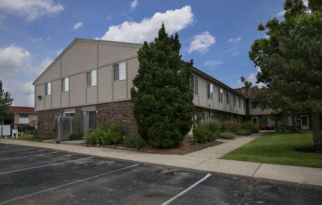 an apartment building in a parking lot with a sidewalk and a tree at Village Club of Rochester Hills, Michigan