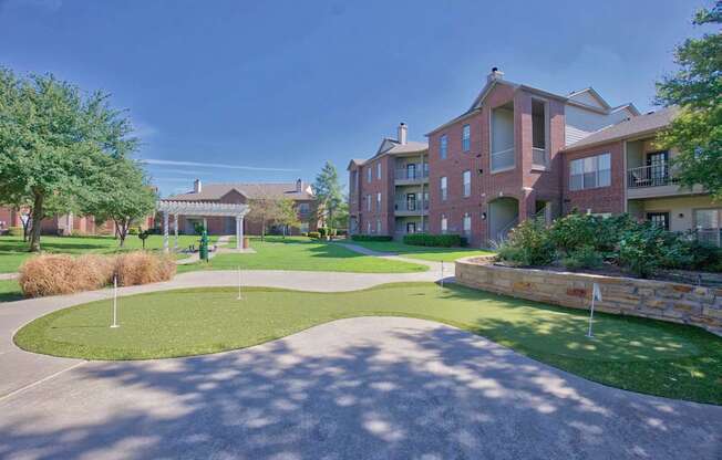 A large grassy area with a stone wall and apartment buildings in the background.