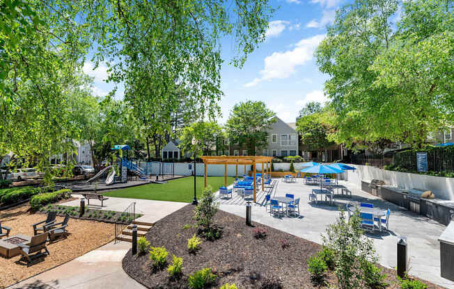 A playground with a slide and a play area with a blue umbrella.
