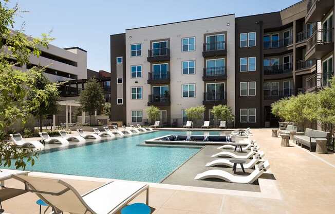 a pool with lounge chairs in front of an apartment building