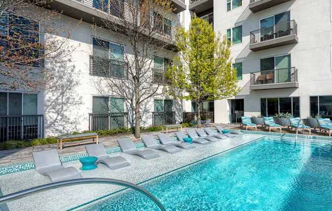 A swimming pool surrounded by lounge chairs in front of apartment buildings.