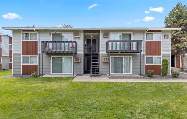 Apartment complex with a green lawn in front A row of apartment buildings with green lawns in front A bedroom with a bed, nightstand, and window at Wildflower, Kennewick, WA 99336..