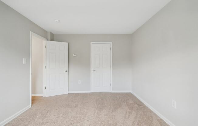 an empty bedroom with two doors and a carpeted floor