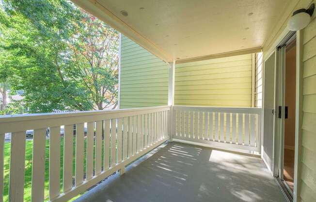 A white porch with a sliding door and a green tree in the background.