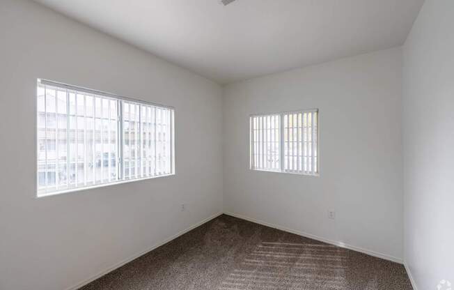 A room with a carpeted floor and two windows.