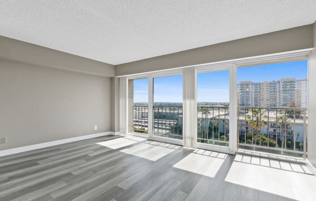 an empty living room with large windows and a view of the city