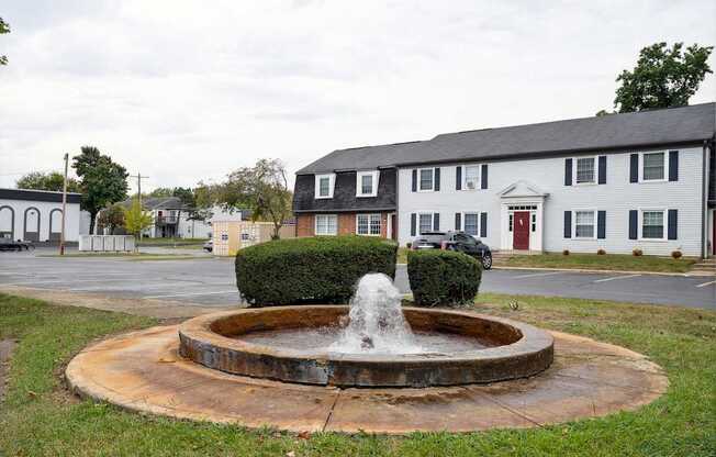 A fountain in the middle of a grassy area in front of a building.