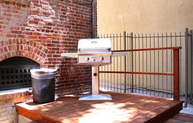 Brookmore Pasadena ca apartments grilling station with a stainless steel grill and trash can on a stained wood deck with railing and brick wall.