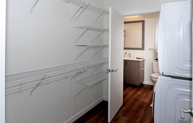 a bathroom with white fixtures and white walls and a closet with shelves and a toilet