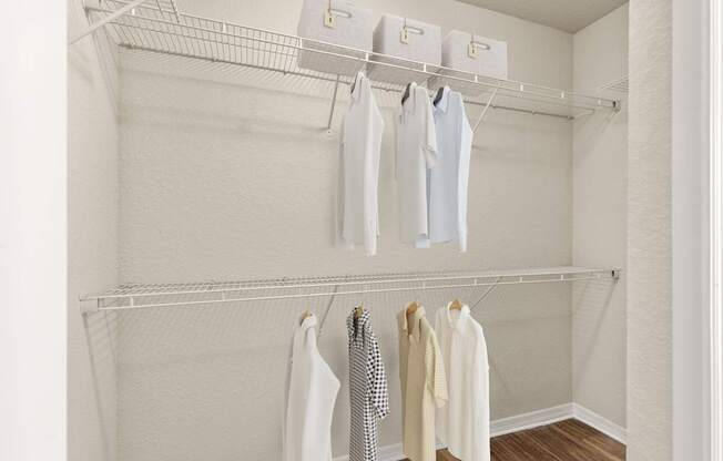 A white closet with clothes hanging on hangers.