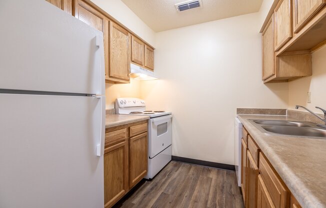 A kitchen with a white refrigerator, wooden cabinets, and a stainless steel sink.