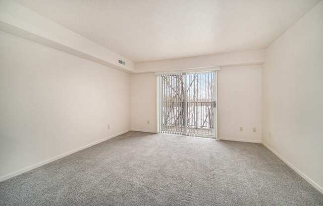 A living room with a carpeted floor and a slider to a balcony at West Hampton Park Apartments in Elkhorn, NE 68022