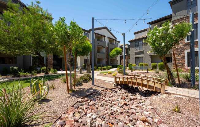 A small bridge crosses a rocky area in front of apartment buildings.