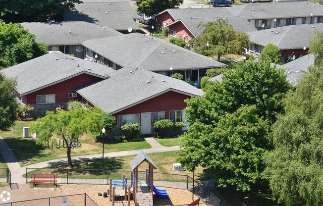 A playground area with a slide and a swing set in front of a red building.