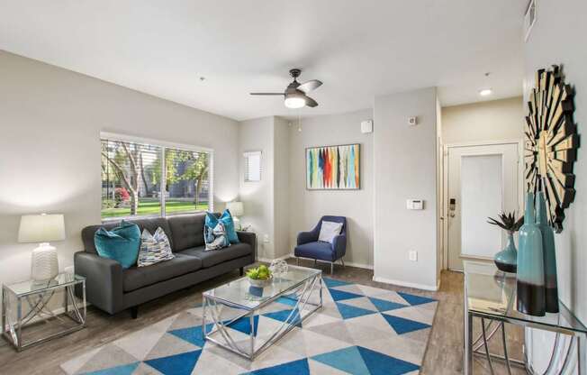 A living room with a grey couch, a blue chair, and a glass coffee table.