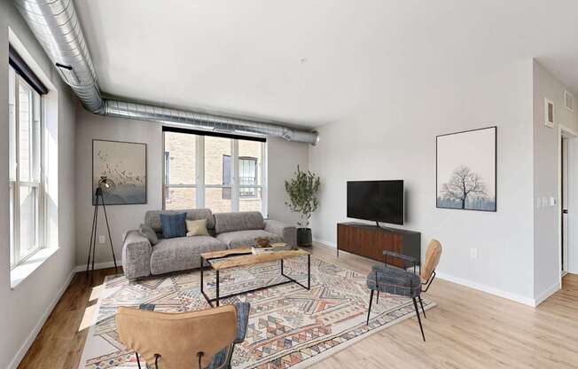 A living room with a grey couch, a rug, a wooden chair and a television.