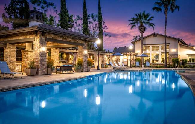 A swimming pool in front of a house with lights on.