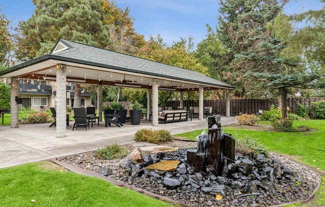 A gazebo is surrounded by a rock fountain and a grassy area.