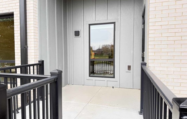 a walk-out patio with black metal railing and a tall window looking into a kitchen