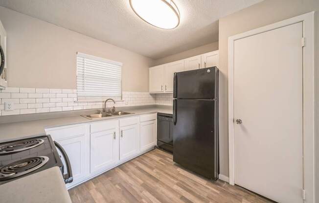 A black refrigerator in a kitchen with white cabinets.