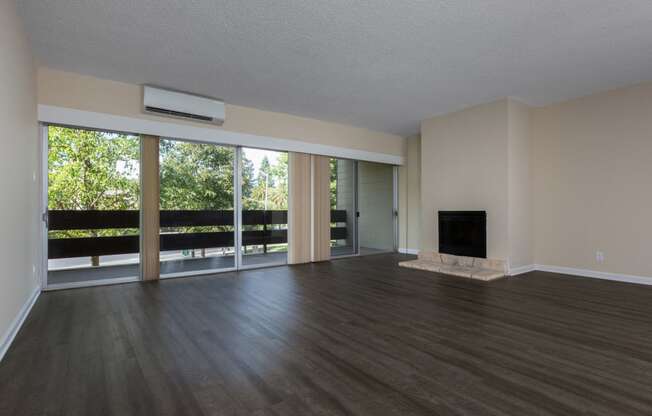 Apartments for Rent Palo Alto, CA - Palo Alto Place - Empty Living Room With High Ceiling, Woodstyle Plank Flooring, AC Unit, Fireplace, And Sliding Glass Doors With Access To Wide Balcony.