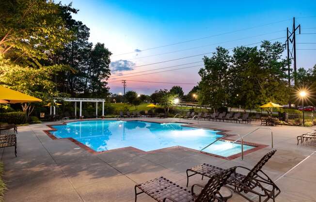 a swimming pool with lounge chairs and umbrellas at dusk