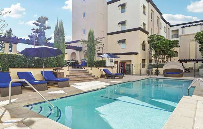 A pool surrounded by chairs and umbrellas in front of a building.