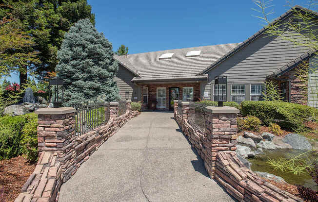 A clubhouse with a grey roof and a grey stone wall in front at Sunset Summit, Rocklin, CA, 95765