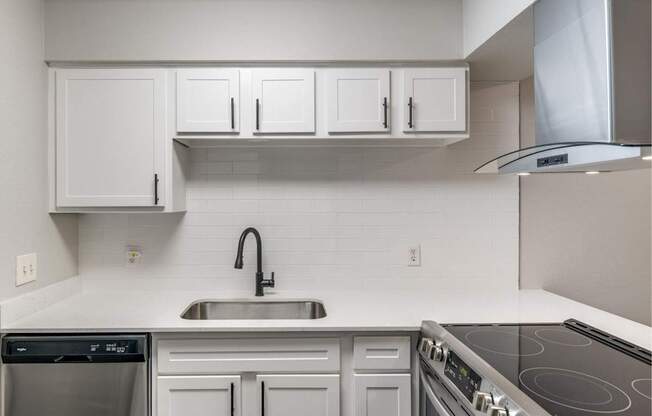 White kitchen counter with undermount sink, white tile backsplash, and electric range.