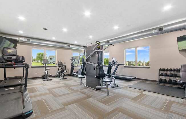 A spacious gym with a variety of equipment and a view of the outdoors through the windows.