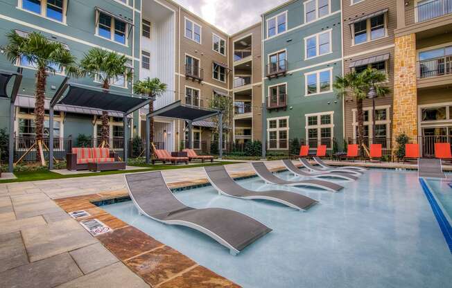 an outdoor pool with chaise lounge chairs and an apartment building in the background