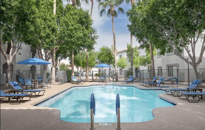 A pool surrounded by trees and chairs.