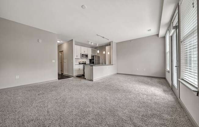 the living room and kitchen of an apartment with a carpeted floor and white walls