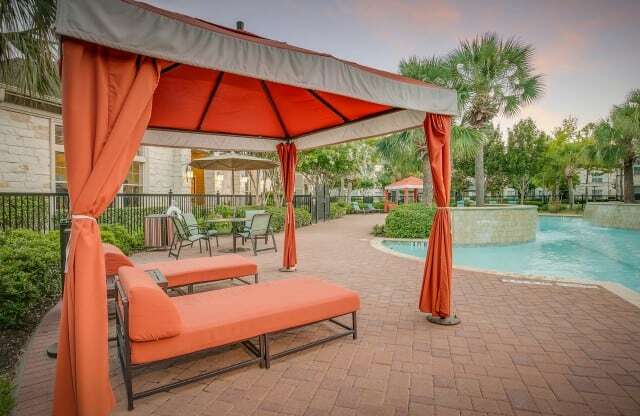 a poolside gazebo with orange curtains and a pool in the background