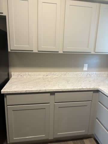 A kitchen with white cabinets and a marble countertop.