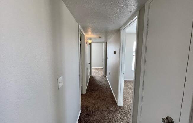 A hallway with a carpeted floor and white walls.