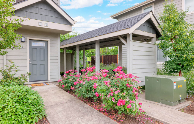 a small gray house with a covered porch and pink flowers