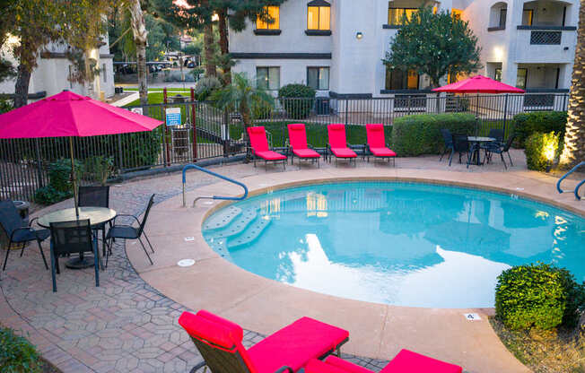 A pool surrounded by red chairs and umbrellas.