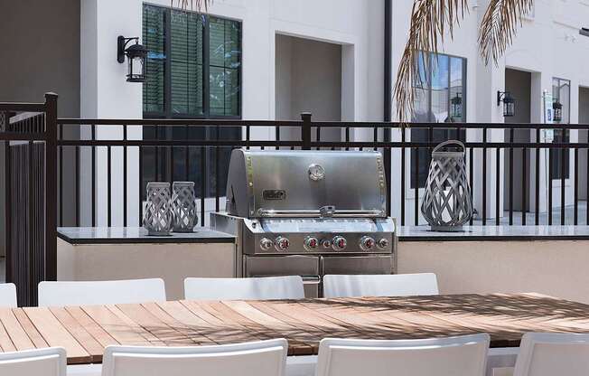 a barbecue grill on a patio with white chairs and a wooden table