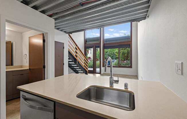 A kitchen with a stainless steel sink and a window overlooking a staircase.