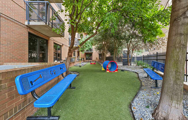 A blue bench is on the grass next to a tree.