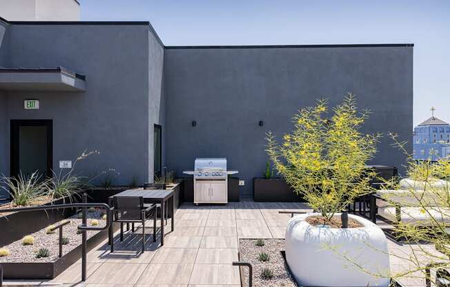 A modern outdoor patio area with a table, chairs, and a tree at Skylar At Sunset Apartments, Los Angeles, CA, 90027