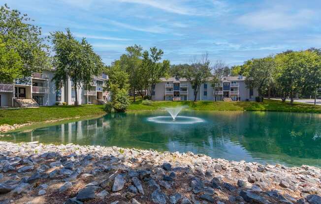 a fountain in the middle of a pond with apartments in the background