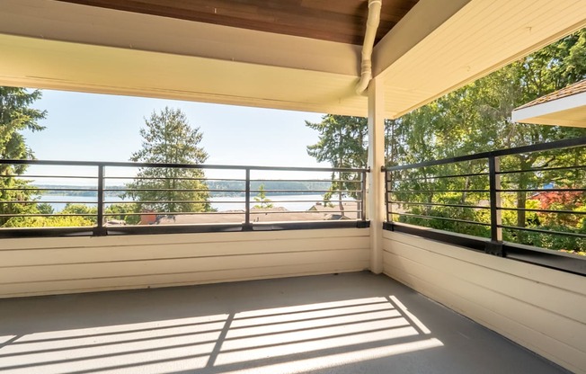 A private covered balcony here at Watercrest with a spacious floor area and sturdy railing, offering scenic views of surrounding trees and water, creating a peaceful and relaxing outdoor retreat.