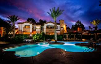 a swimming pool at night at an apartment complex with palm trees