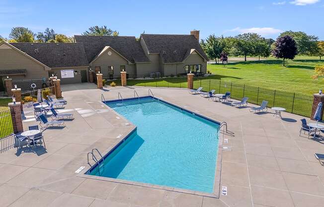 A large swimming pool surrounded by a concrete patio and lounge chairs at Oak Shores Apartments in Oak Creek, WI