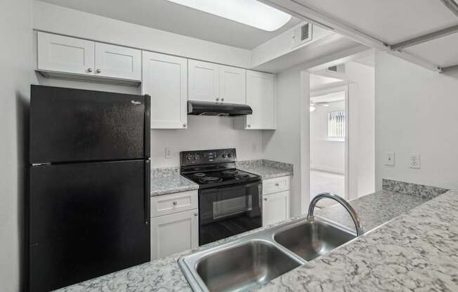 A black refrigerator is in a kitchen with granite countertops.