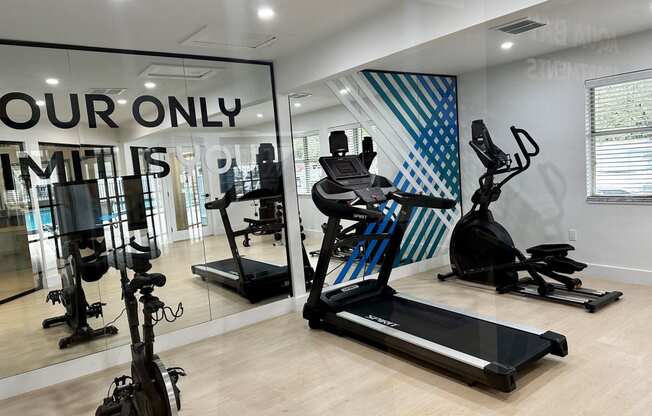 A gym with cardio equipment and a large window with your only limits signage on it at Aqua Bay Apartments in Naples, FL 34116