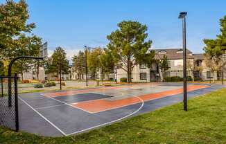 a basketball court with trees and apartments in the background